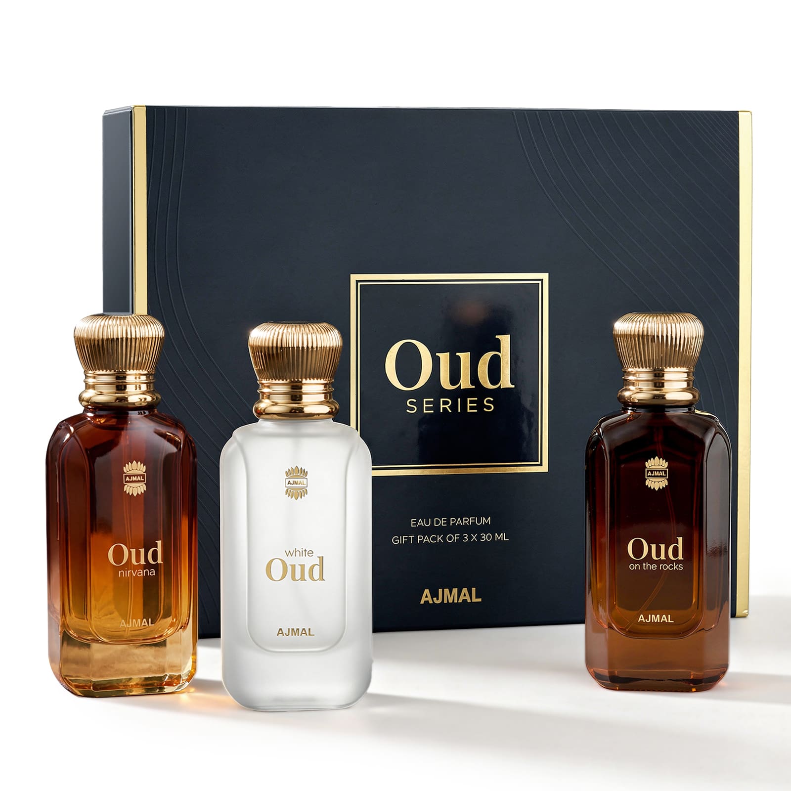 AJMAL Oud Series gift set featuring three fragrance bottles in front of a dark navy blue box with gold trim. The set includes two amber-brown bottles and one frosted white bottle, all with ribbed gold caps and gold lettering.